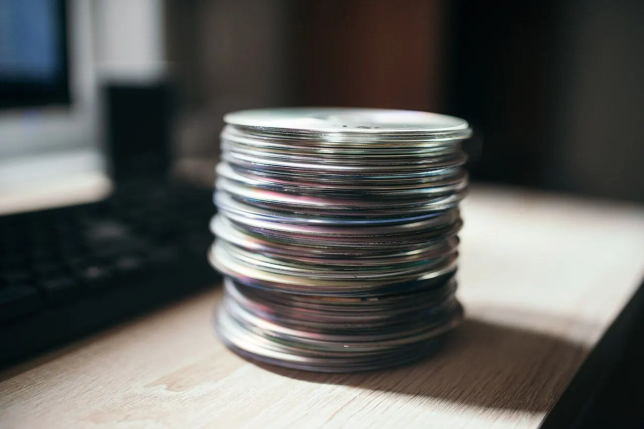 Stack of CDs resting on a wooden table near a computer keyboard in a home office setting